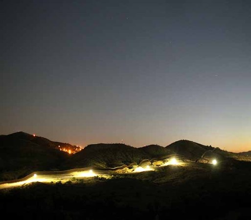 NOGALES, AZ - JUNE 22: Flood lights illuminate the U.S. border fence with Mexico at dusk on June 22, 2011 near Nogales, Arizona. The Pentagon recently extended the deployment of some 1,200 guardsmen who were deployed last year to assist with border security on the U.S.-Mexico border until September 30. Soldiers at Early Identification Team (EIT) observation posts in Nogales work 24 hour shifts, each taking turns resting for 4 hours during the night. The National Guard troops are strictly on surveillance duty, although they are armed and have been credited with helping U.S. Border Patrol agents arrest up to 17,000 illegal immigrants crossing into the United States. (Photo by John Moore/Getty Images)