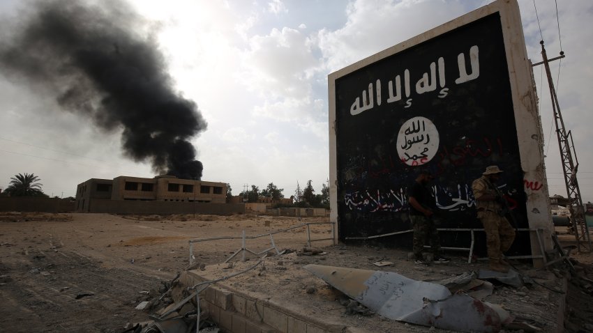 This Nov. 3, 2017, file photo shows Iraqi fighters of the Hashed al-Shaabi (Popular Mobilisation units) stand next to a wall bearing ISIS group flag as they enter the city of al-Qaim, in Iraq's western Anbar province near the Syrian border as they fight against remnant pockets of Islamic State group jihadists