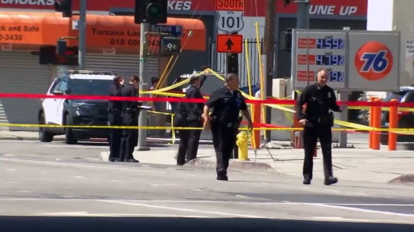 Police officers walk near crime scene tape in front of a 76 gas station