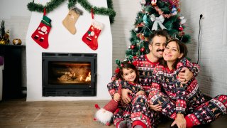 Una familia vestidos con pijamas navideños delante de la chimenea y un árbol de Navidad.
