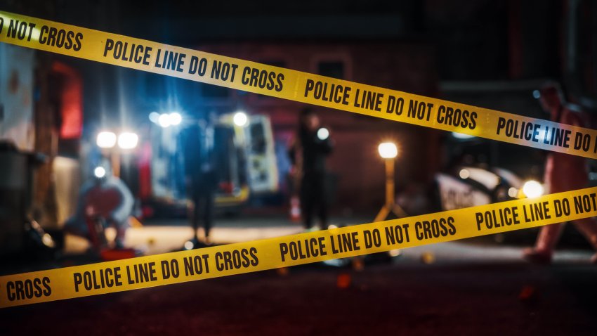 Crime Scene at Night: Crime Scene Investigation Team Working on a Murder. Female Police Officer Briefing Detective on the Victim’s Body. Forensics and Paramedics Working. Cinematic Shot