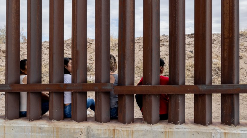 Grupo de mexicanos mirando a través del muro fronterizo internacional entre Chihuahua México y Texas, EEUU.