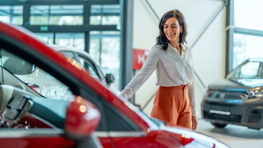 Businesswoman looking for a new car, standing next to a new SUV indoors at a car dealer