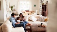 Young Hispanic family sitting on sofa reading a book together in the living room, seen from doorway