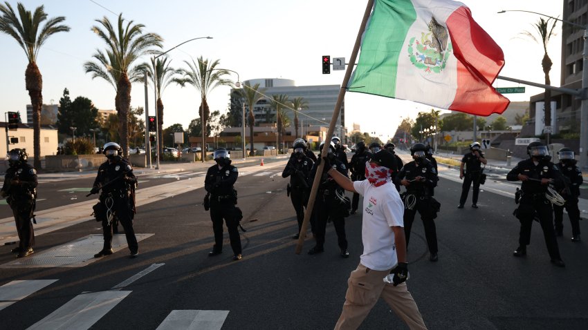 A person holds a Mexican flag outside the United States Citizenship and Immigration Services (USCIS) Santa Ana Field Office after reports of Immigration and Customs Enforcement (ICE) raids in Santa Ana, California, on June 9, 2025. The City of Santa Ana released a statement on Facebook acknowledging the ICE activity and the “fear and uncertainty” it would cause for some community members. President Donald Trump’s administration said on June 9 that it was sending 700 US Marines and thousands more National Guard troops to Los Angeles, sparking a furious response from California’s governor over the “deranged” deployment. (Photo by Patrick T. Fallon / AFP) (Photo by PATRICK T. FALLON/AFP via Getty Images)